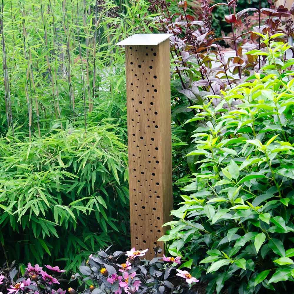 Bee house BEE TOWER 65 in smoked oak with holes directly into the wood, standing in garden