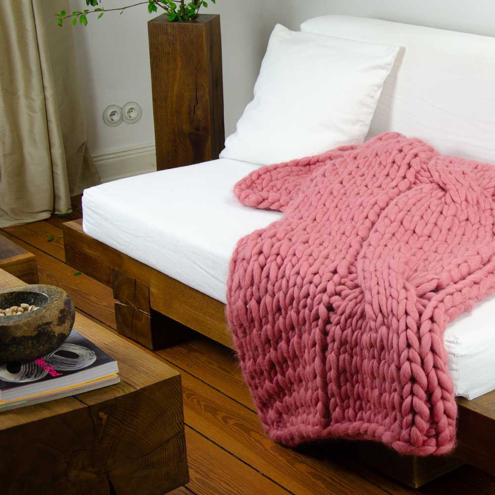 Chunky knit blanket FLUF with one-sided braid in rose laid over sofa