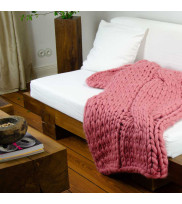 Chunky knit blanket FLUF with one-sided braid in rose laid over sofa